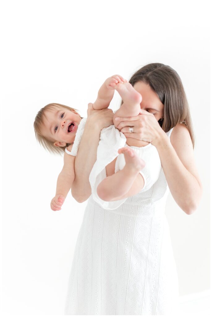 A Nova Studio Photography photoshoot of a mother snuggling her baby and kissing her on the leg