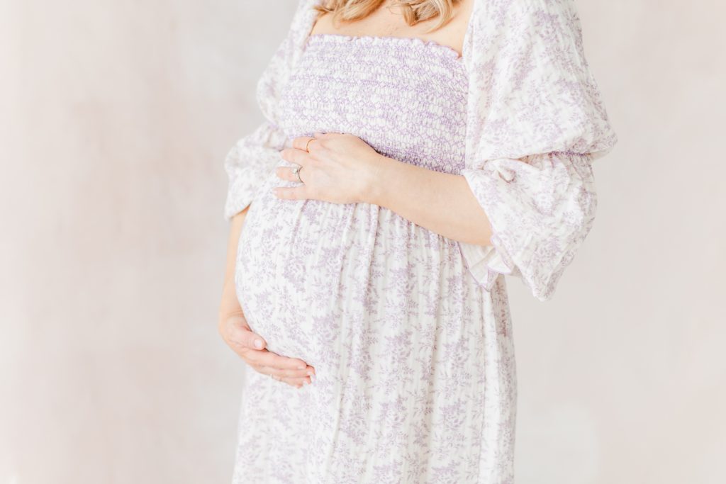 A pregnant mother holding her baby bump in front of a hand painted canvas