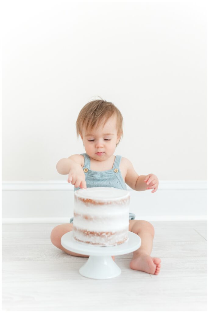 A cute baby wearing a blue bubble romper playing with a smash cake by DC Baby Photographer