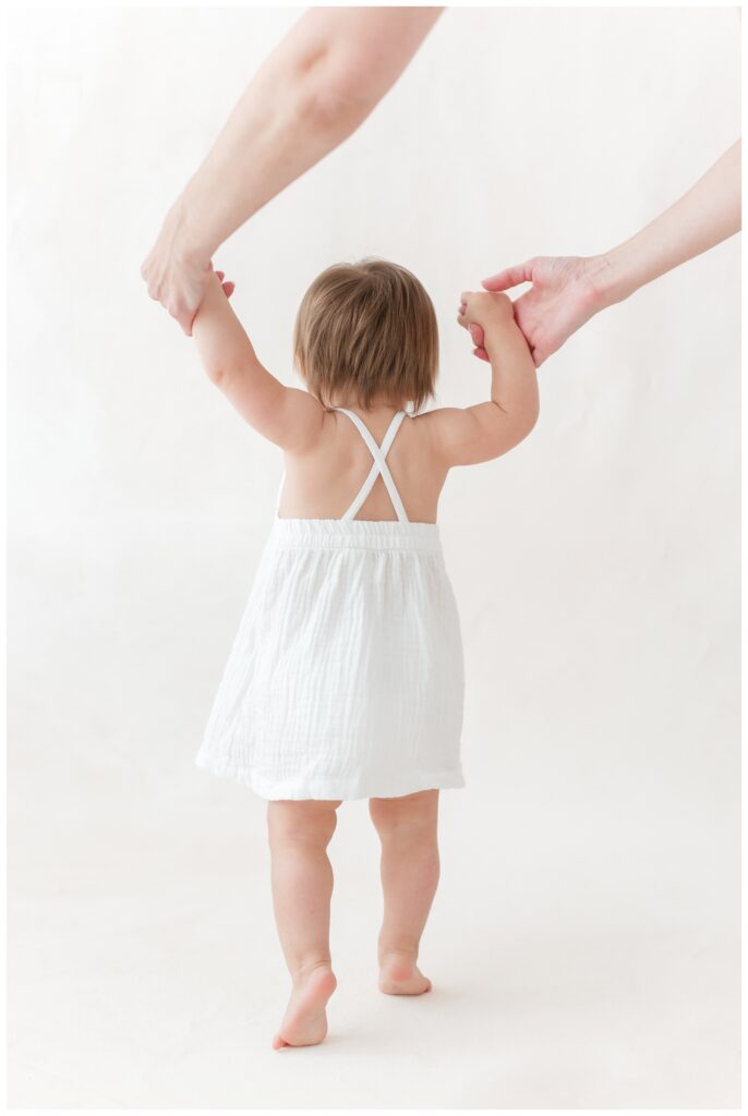 A mother helping her baby walk on a hand painted canvas backdrop by DC Baby Photographer