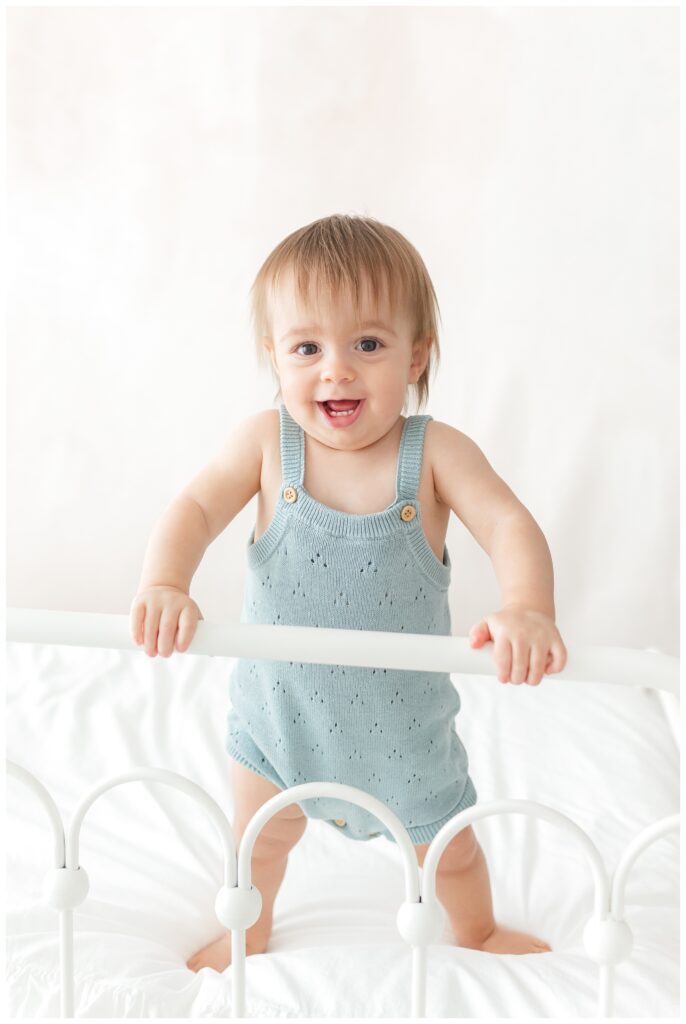 A baby playing on a bed and smiling at the camera by DC Baby Photographer