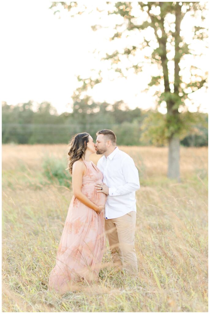 A pregnant couple kissing outside in a field at sunset for their Northern Virginia Maternity Photographer